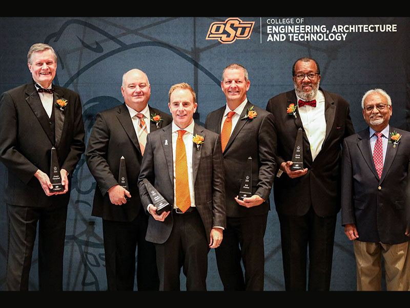 A group of individuals dressed in formal wear stand in front of a black CEAT photo backdrop.