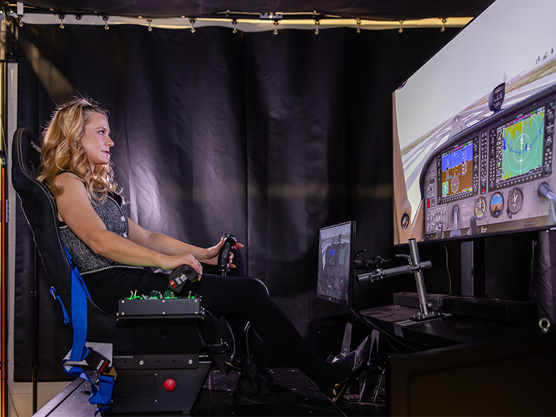 Ainsley Kyle sits in the seat of a flight simulator in a lab setting in the Advanced Technology Research Center at Oklahoma State University.