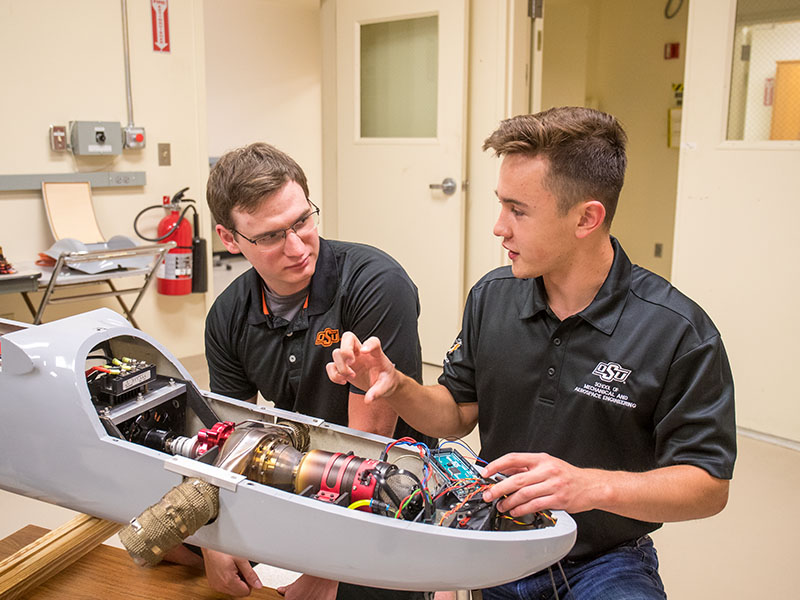 Two graduate students discuss the mechanics of a disassemble UAV that rests upon the table in front of them.