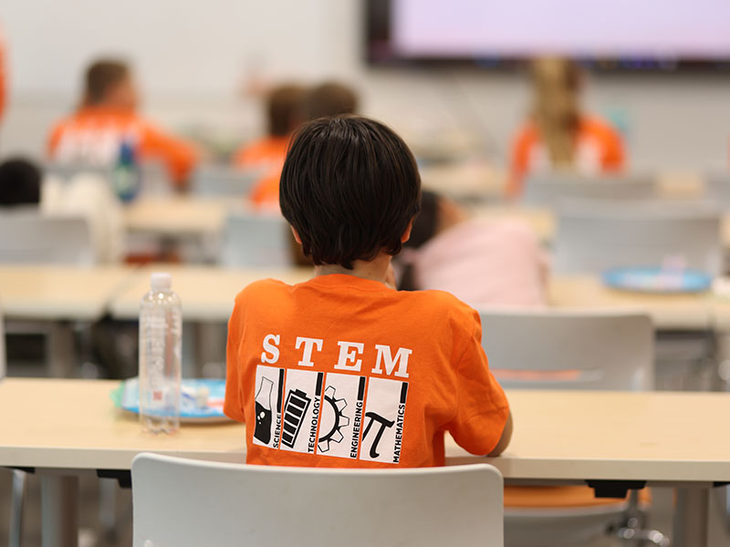 A young student sits at a desk during an experiment presentation.