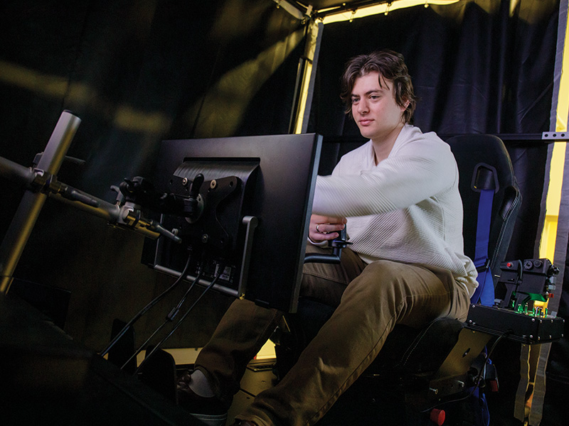 Brock Rouser sits in the seat of a flight simulator in a lab setting in the Advanced Technology Research Center at Oklahoma State University.