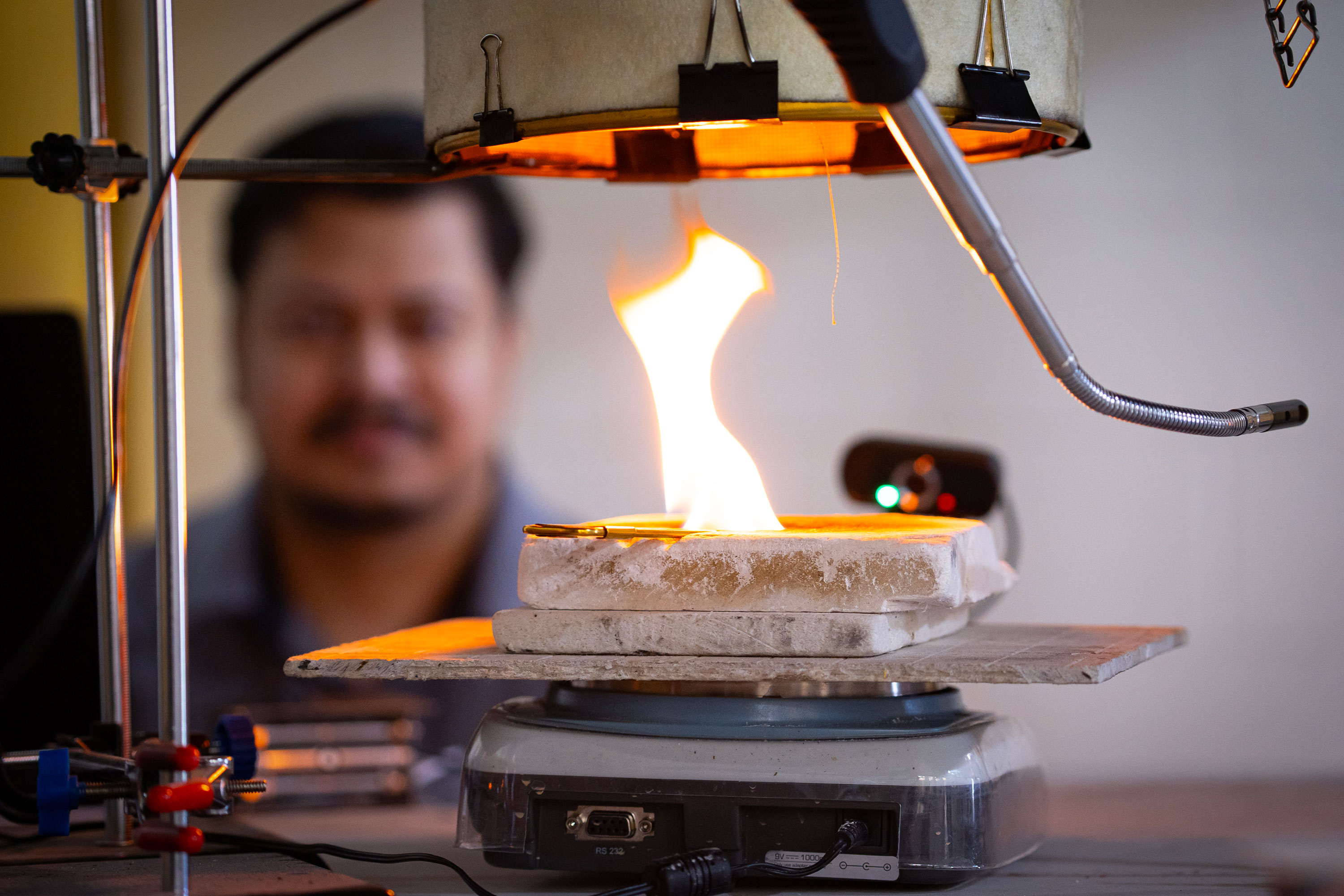 LET IT BURN | Sayak Nandi (left) observes the behavior of nanofabric through lab-simulated smoke exposure before it is deemed ready for field testing, where it is layered within the PPE jacket worn during an open burn (right). The jacket is later deconstructed to evaluate the filtration performance of the nanofibers after functional use.