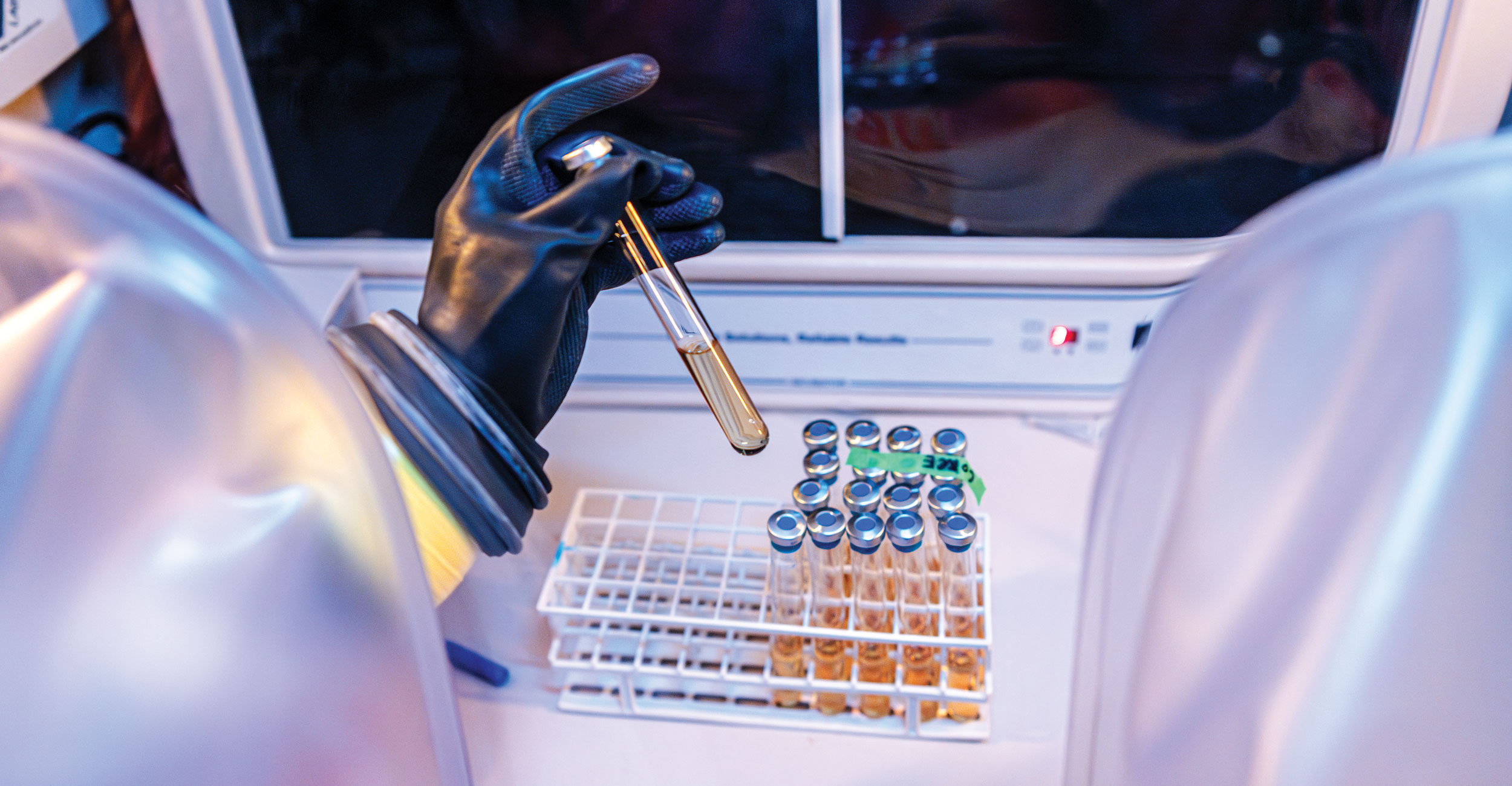 Hands wearing rubber gloves pick up test tubes in a microbiome lab