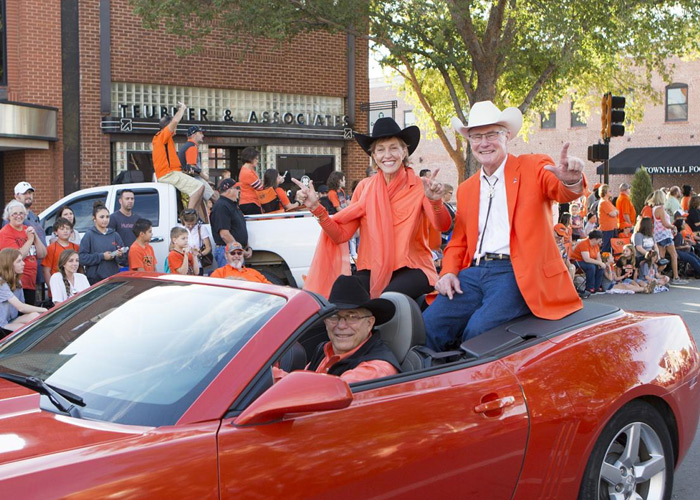 President Burns Hargis and First Cowgirl Ann Hargis on red car at Homecoming parade