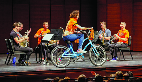 Rebecca Young, principal viola for the New York Philharmonic, rides a bike around Brass Quintet members Ethan Bensdorf, Richard Deane, Alan Baer, Colin Williams and Christopher Martin.