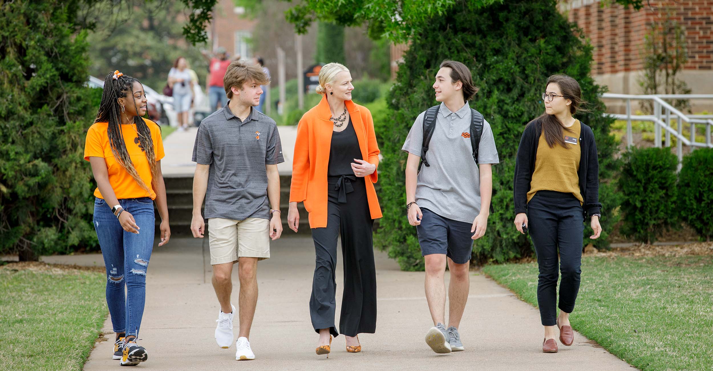 President Kayse Shrum walks down a sidewalk talking to students.