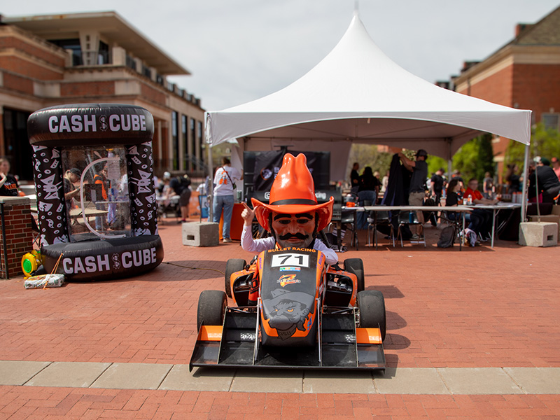 An outdoor event with a small orange and black race car numbered 71 parked in front of a white canopy tent. 