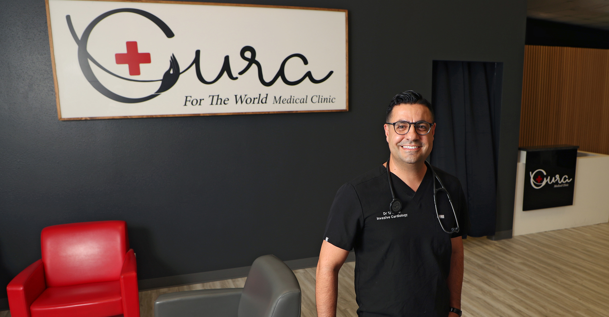 A medical professional stands in a modern clinic lobby with red and gray chairs. Behind them is a large sign displaying the 'Cura' logo and the text 'For The World Medical Clinic.' Another sign with the same logo is visible near the reception area in the background.