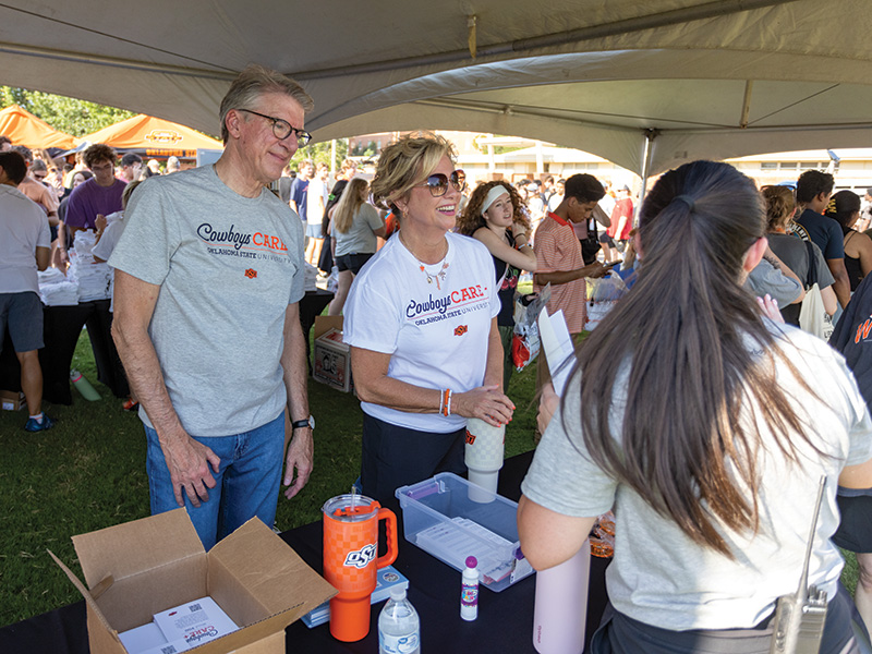 A man and a woman in gray shirts that say "Cowboys Care" hand out shirts to students.