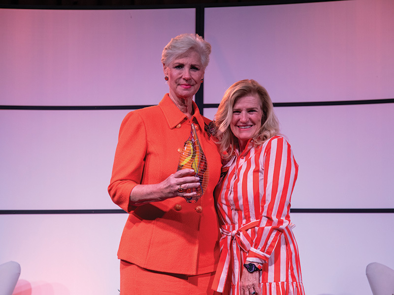 Two people stand together on a stage during an awards event, with one holding a glass award while both pose for a commemorative photo.