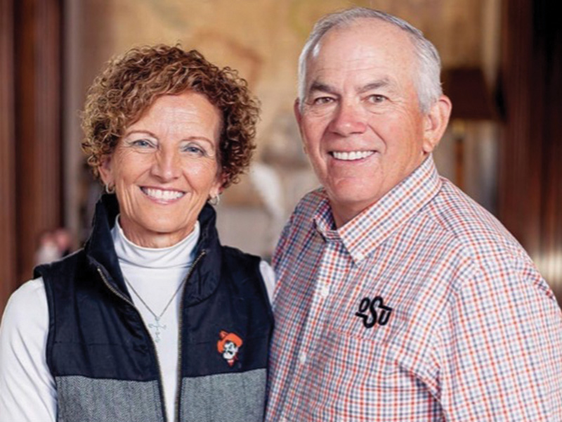 Two individuals stand side by side indoors, dressed in business casual attire and posing for a portrait, with one wearing an OSU-branded shirt.