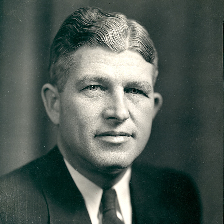 Person in a formal suit and tie with neatly combed hair, shown in a black-and-white portrait.